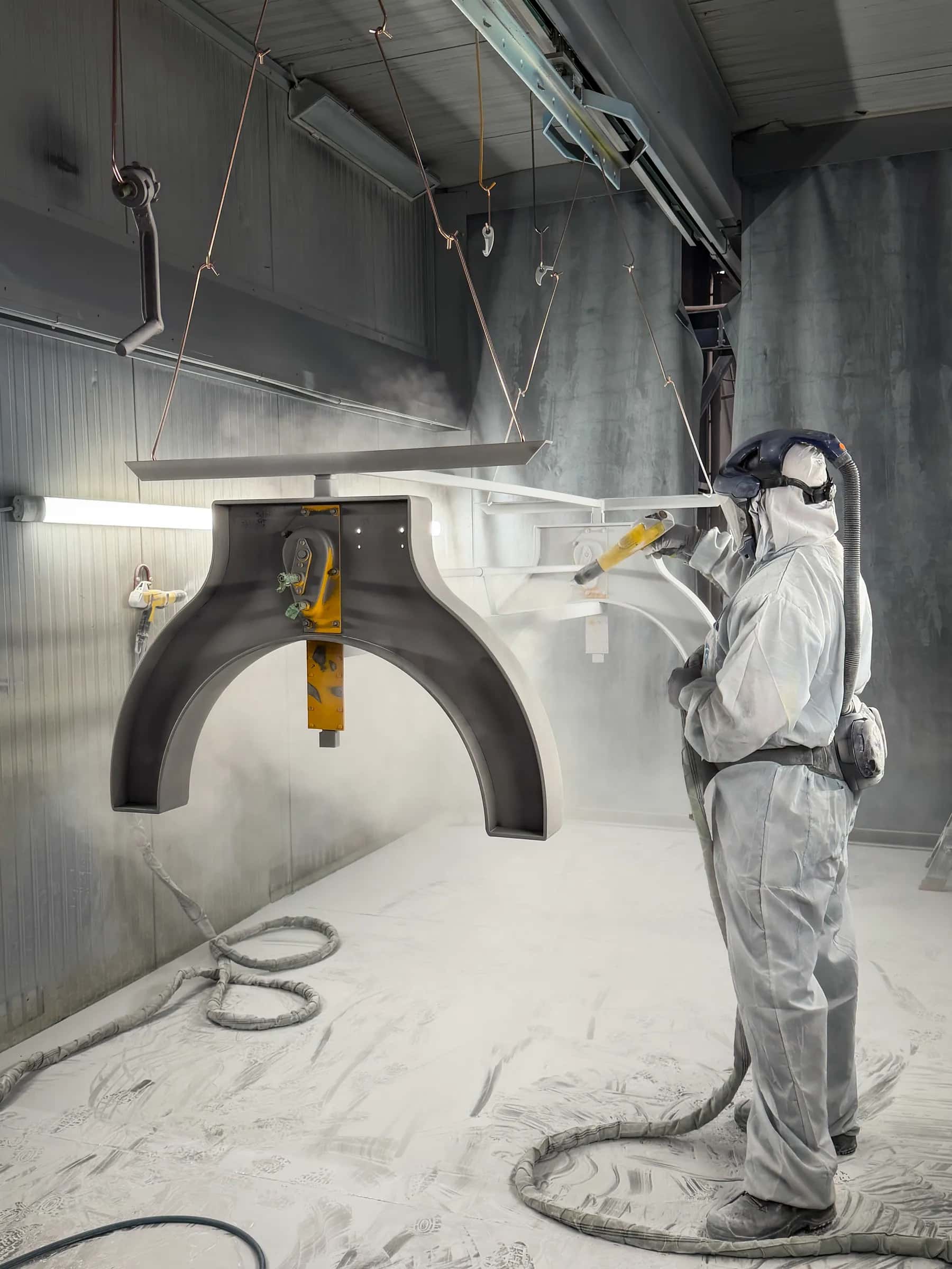 Steel table base being coated by a worker in protective clothing in the workshop