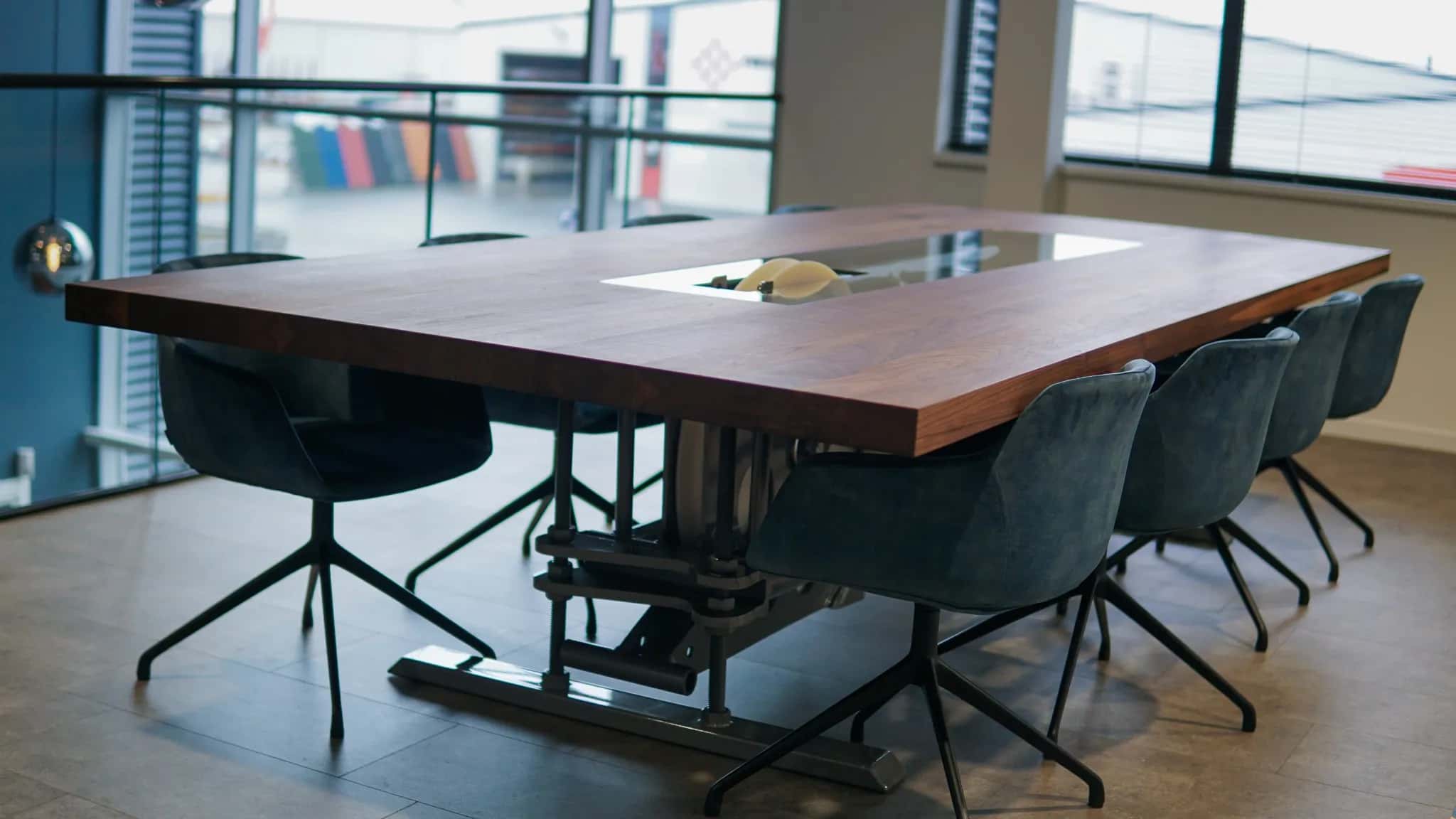 Oak conference table on a black steel base with green chairs in the Gouwe Leeuw office overlooking the workshop