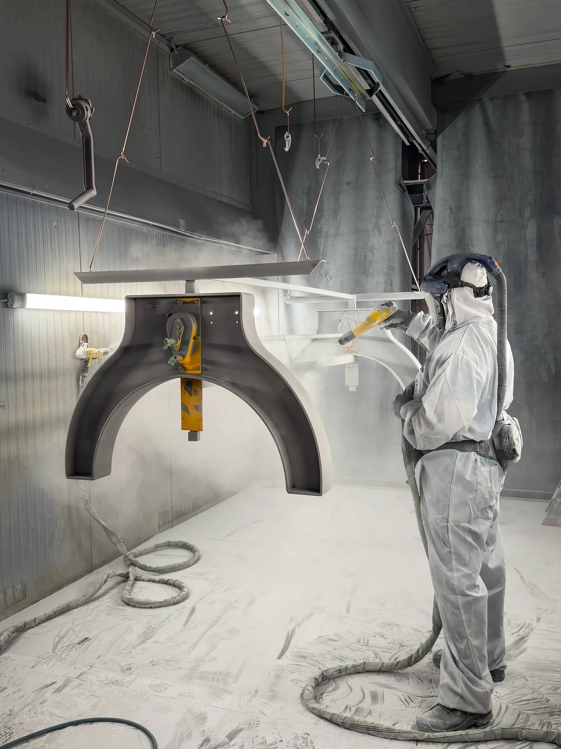 Steel table base being coated by a worker in protective clothing in the workshop