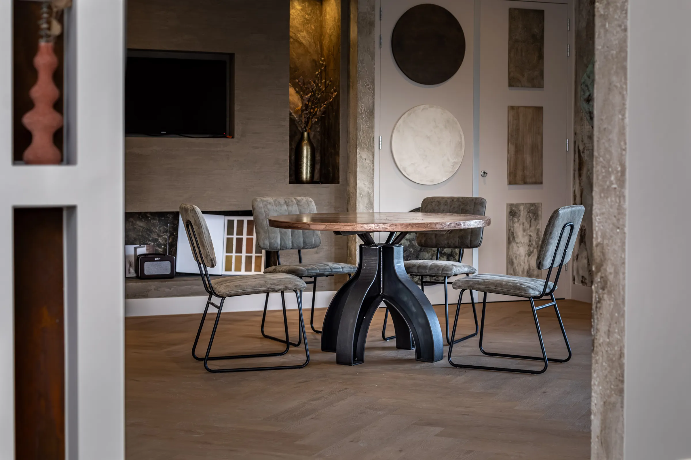 Round oak table on a black double arch base in a showroom with a concrete look wall