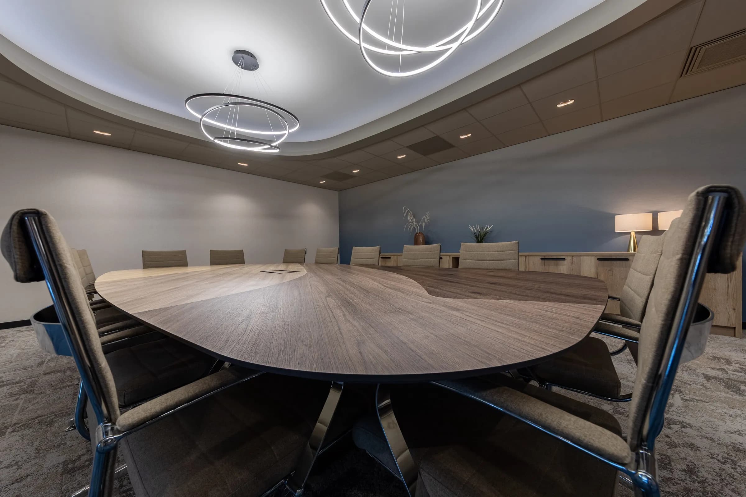 Boardroom with a large oval dark wood table on a steel spider base under round ceiling lights at Kramer Seafood