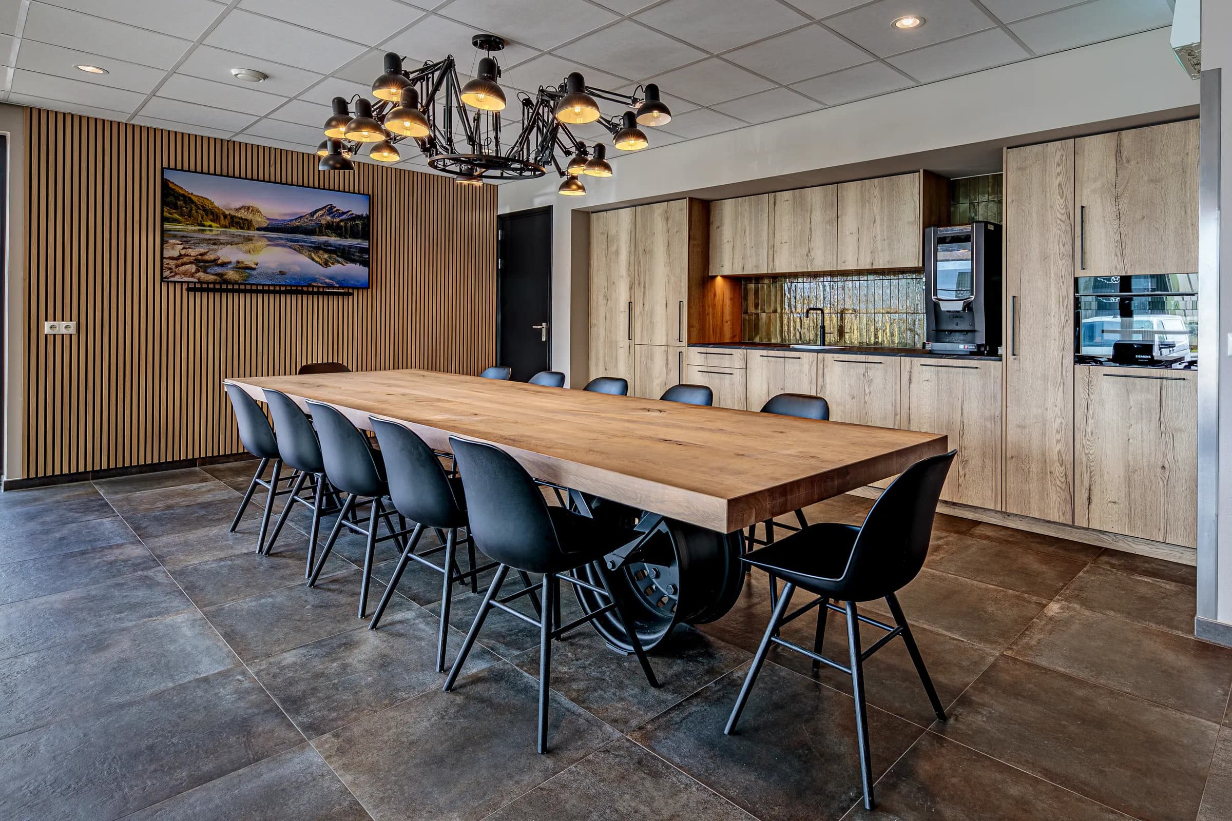 Canteen with a long light table on a car rim base, black chairs and a wooden slat wall at Van Wieren in Emmeloord