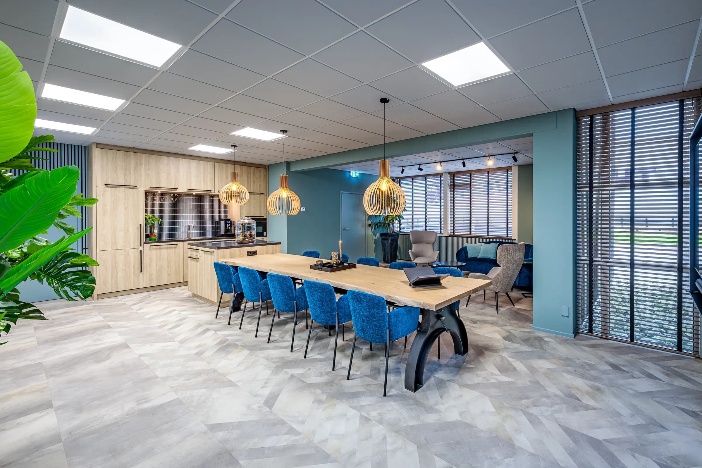 Long light oak table on a black cast iron column base with blue chairs and plants in the Wiz Arts office
