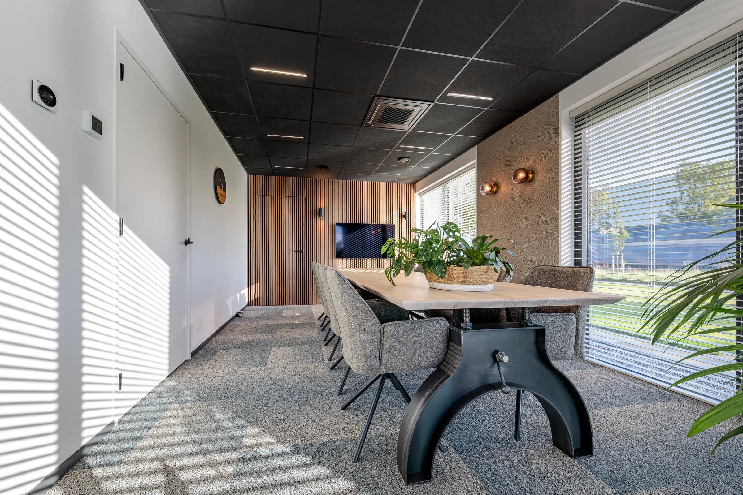 Light oak conference table on a cast iron column base with grey chairs and plants in the Advies en Kies office